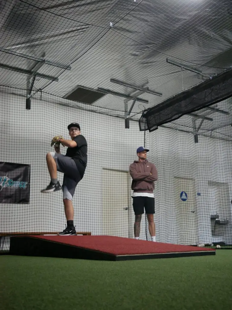 BAP pitcher in his windup as a coach watches